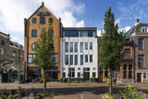 Voorgevels van diverse panden aan de De Ruijterkade in Amsterdam, waaronder het SMC-gebouw en een wit modern pand tussen historische bebouwing.